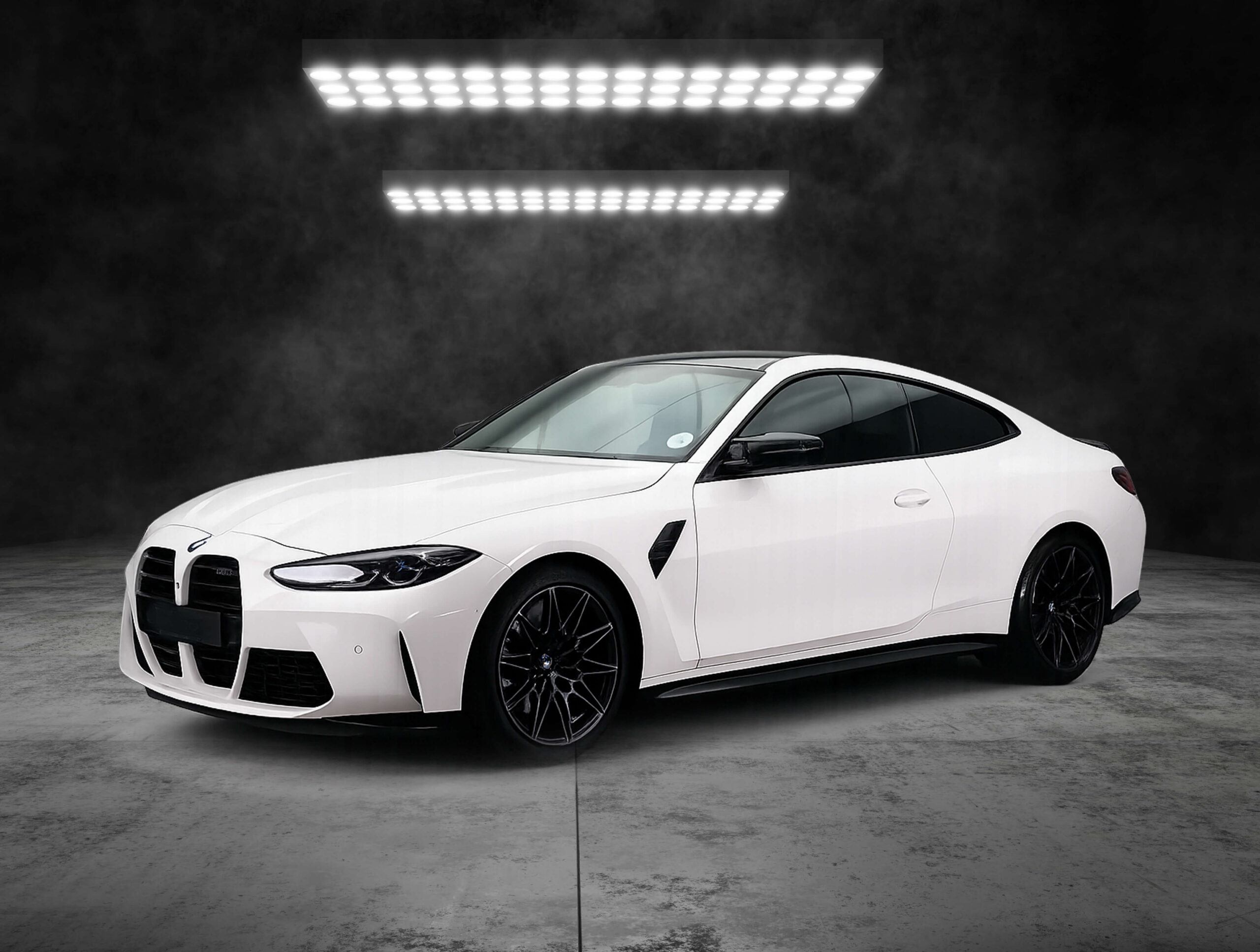 White sports car in a dark studio, illuminated by two rows of bright overhead LED lights.