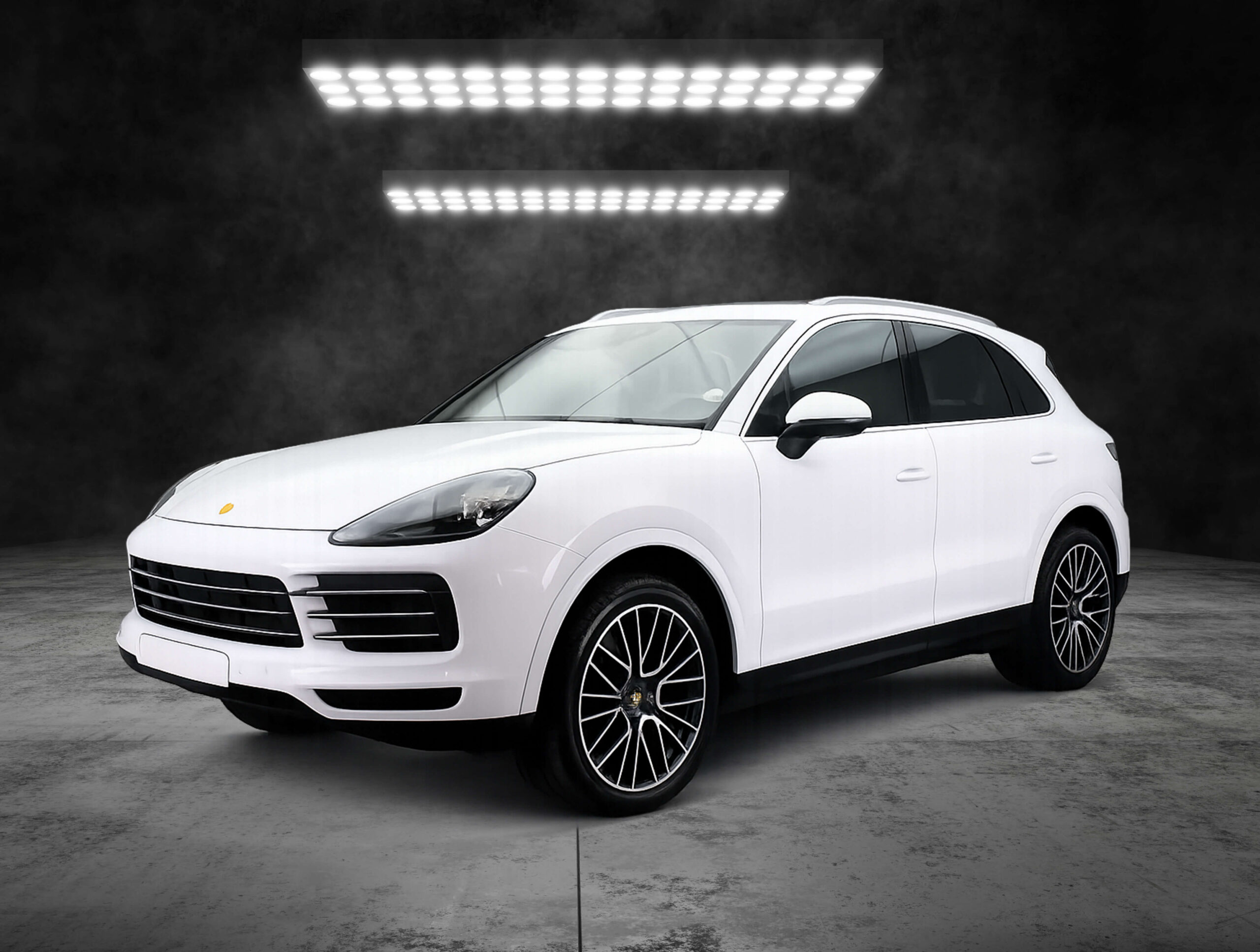 White SUV photographed in a studio setting with bright overhead lights and a smoky backdrop, front-right angle showing the grille and large alloy wheels.
