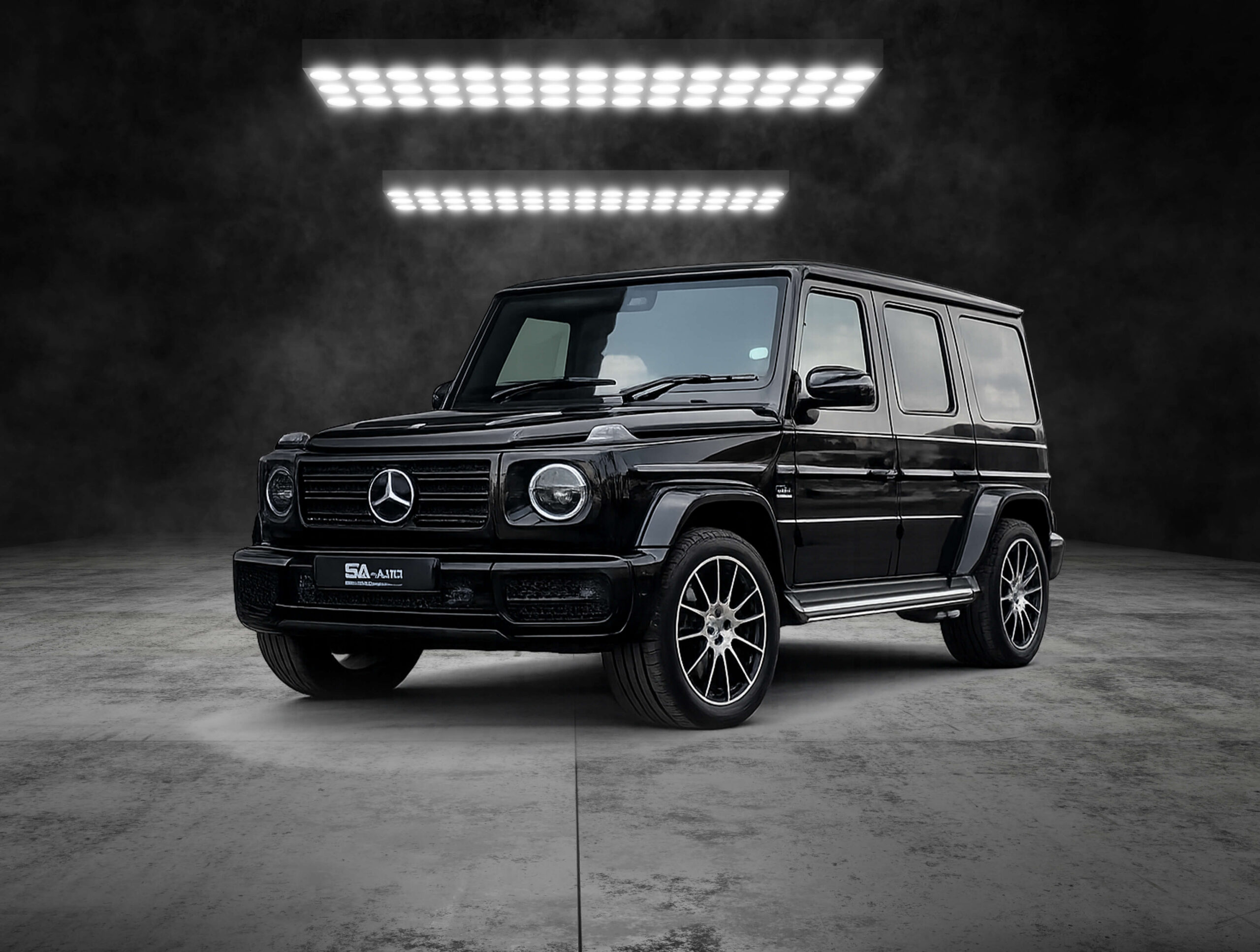 Front three-quarter view of a black Mercedes-Benz G-Class SUV under bright studio lights against a dark background.