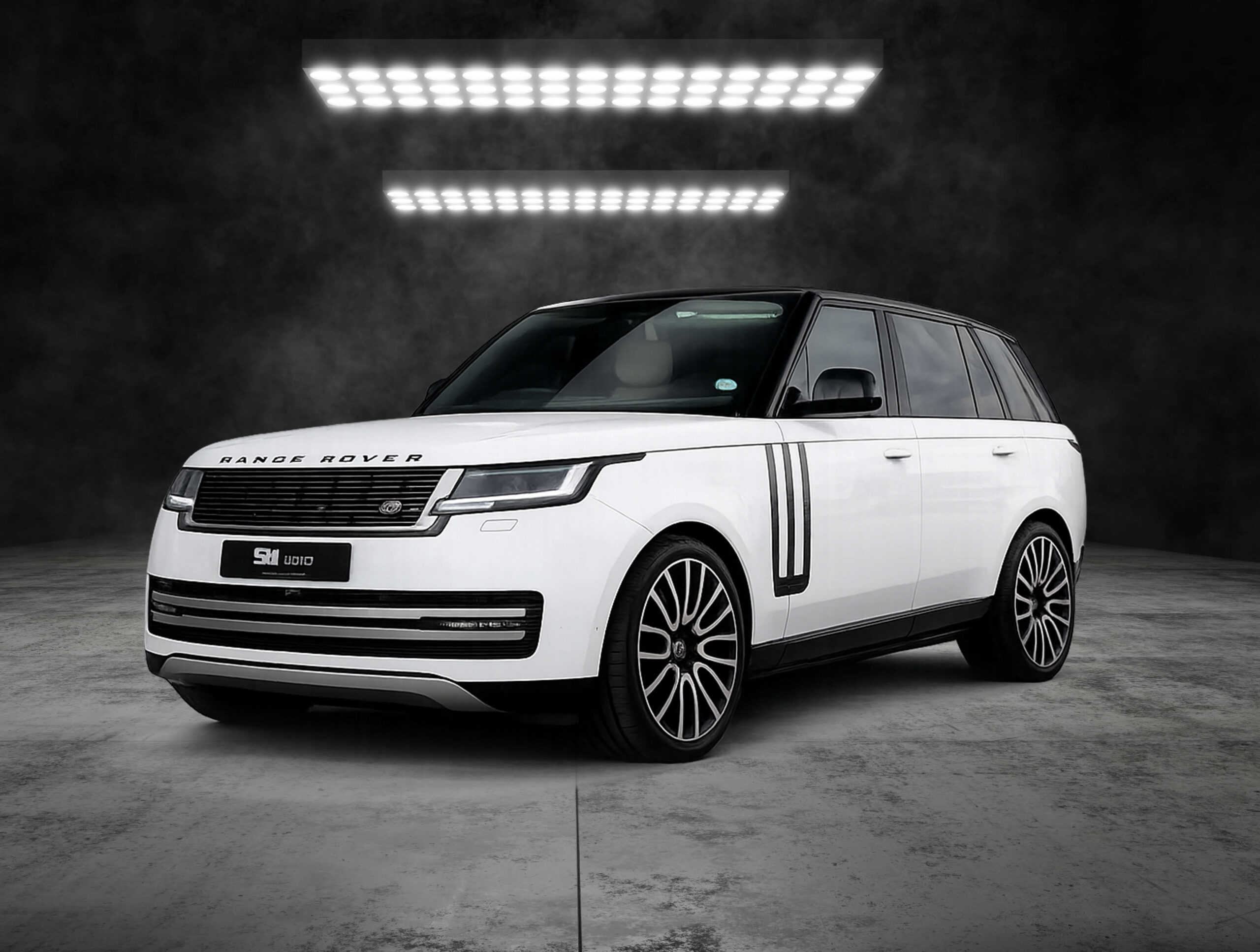White Range Rover SUV in a dark studio setting with bright overhead LED lights, shown from a front-side angle.