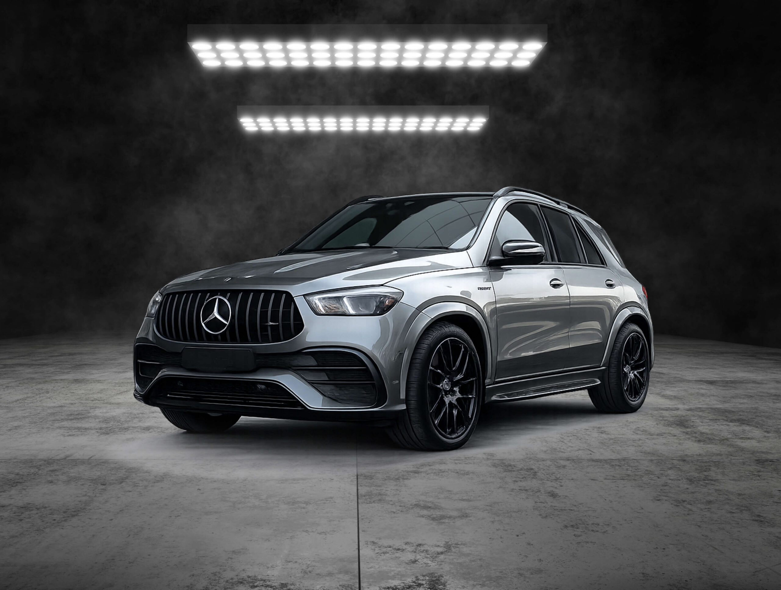 Silver Mercedes SUV in a dim studio with two hanging LED light panels above, front three-quarter view.
